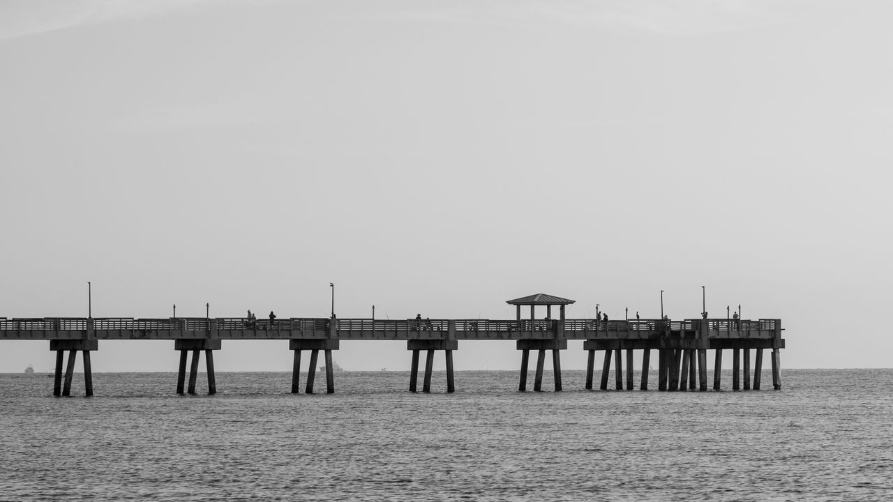 Scenic black and white view of a pier extending into the ocean with people walking.