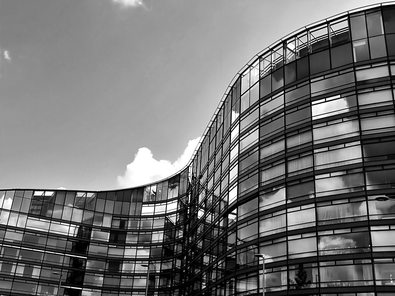 Modern black and white photo of a curved skyscraper with reflective glass windows.